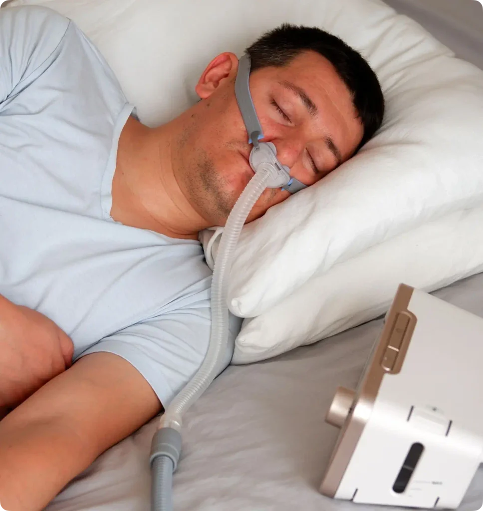 Man sleeping in a bed with a sleep apnea device attached.